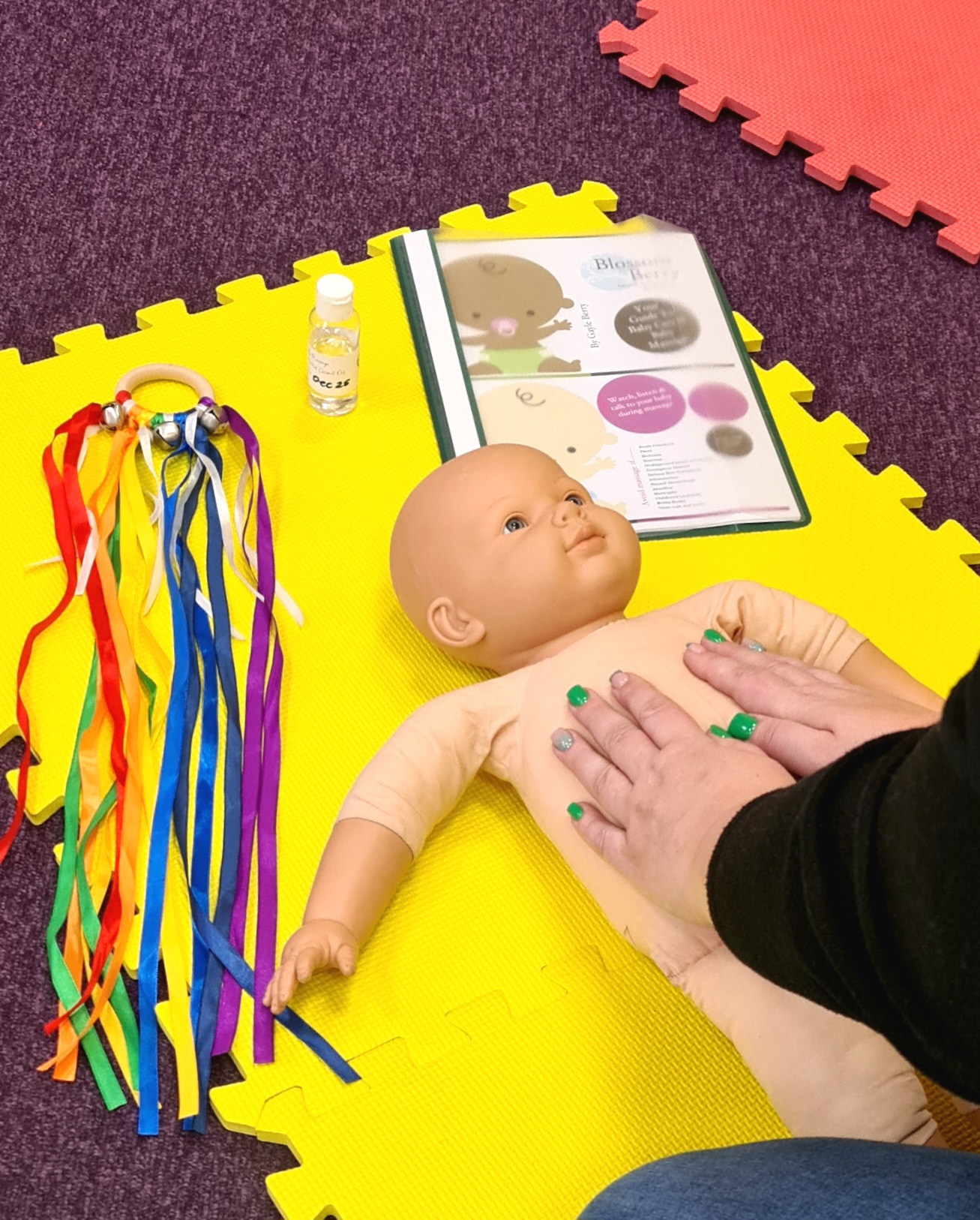 Baby massage doll on mat with instruction booklet and bottle of oil